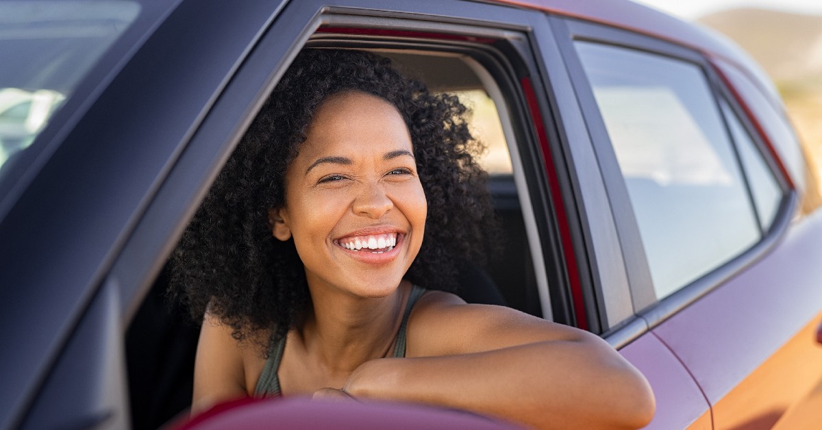 Woman driving a red car while smiling