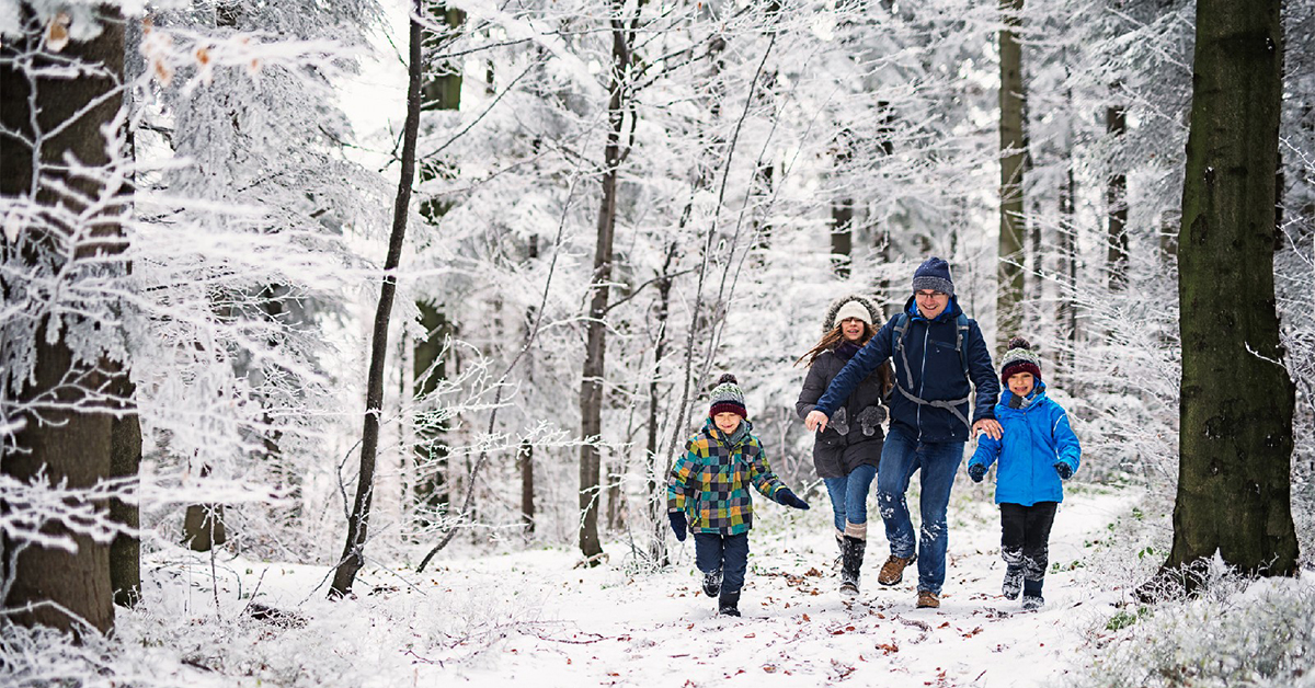 Father with three kids running in beautiful winter forest. The little girl is aged 10 and her brothers are aged 7. Cold winter day