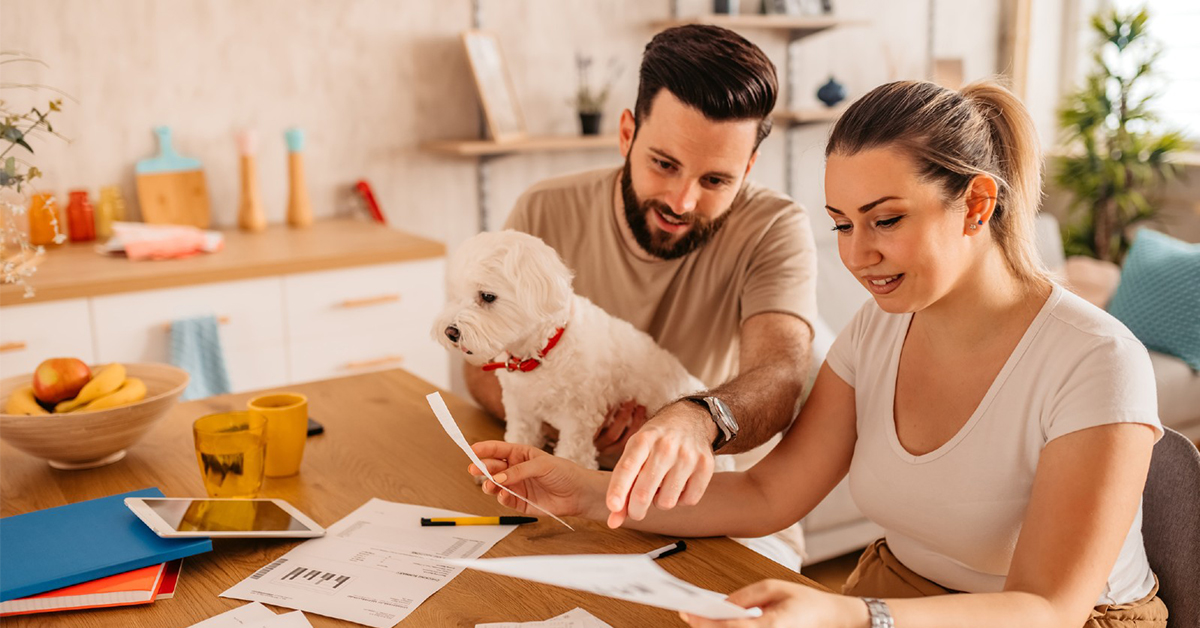 Young heterosexual couple sitting in their living room and checking their life insurance policy. Man holding cute toy dog in his lap.